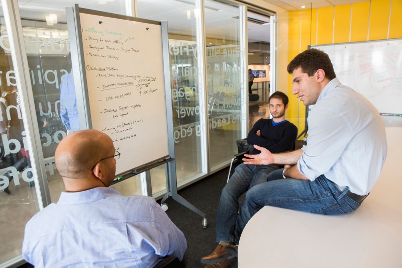 Three VDC coworkers gather around a whiteboard to discuss business strategy.